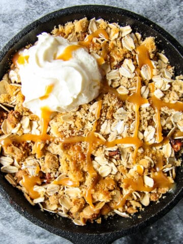 Air fryer apple crisp in a cast iron pan, topped with a dollop of whipped cream.