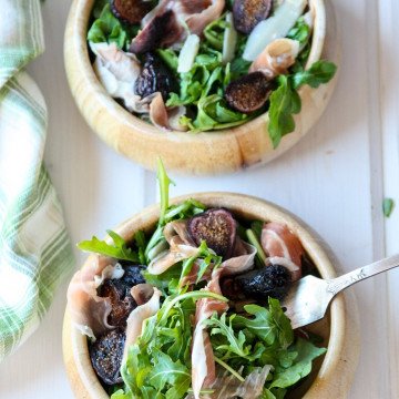 A bowl of salad on a plate, with Arugula