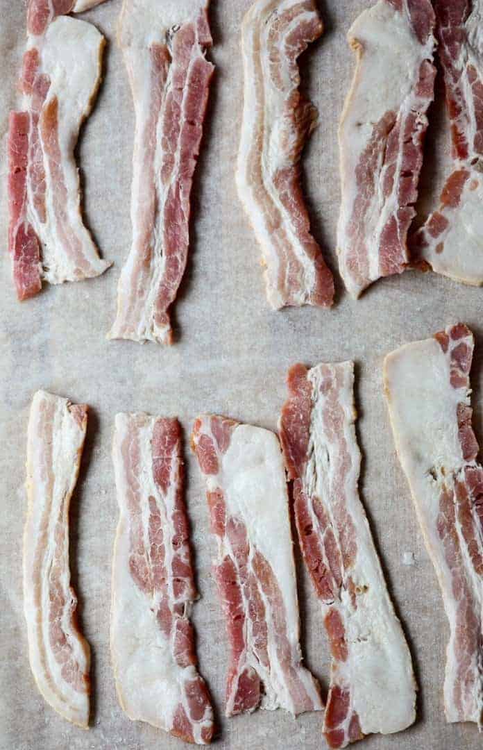 Ten strips of raw bacon on a baking sheet