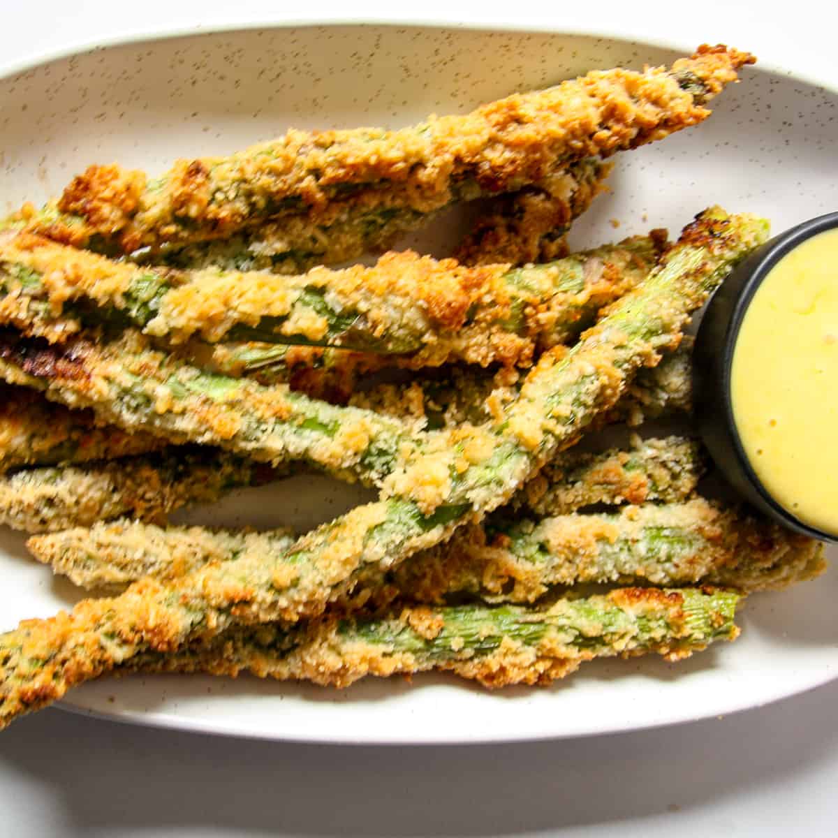 Air fried asparagus on a speckled white plate.