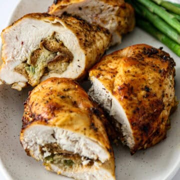 Four stuffed chicken breast halves on a white plate.